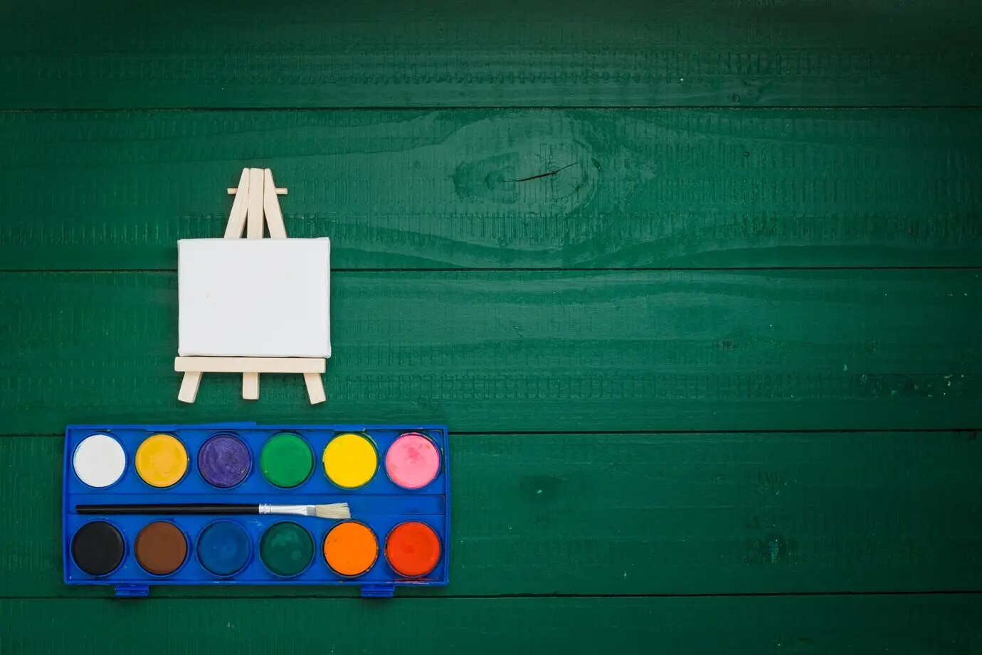 Aquarellset und Miniaturstaffelei vor grünem Hintergrund